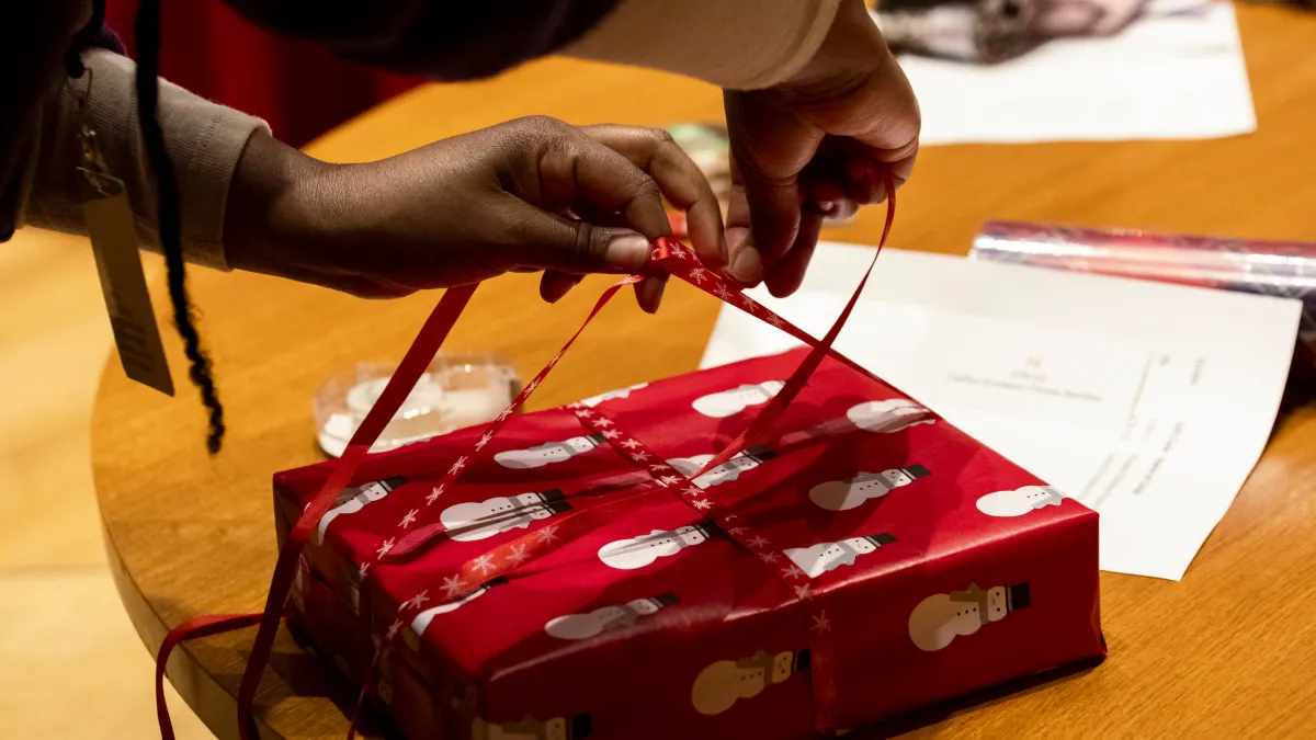 A person wraps a gift with ribbon.