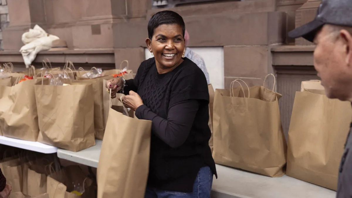 A lady distributes grocery bags to people in line.