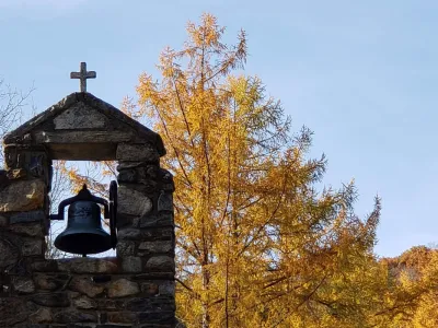 Chapel's cross and bell are framed by yellow leaves under a blue sky