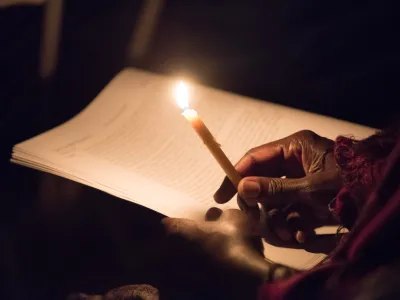 A person holds a candle to read the prayer. 