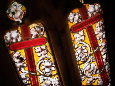 Two red crosses surrounded by a white flowering vine over a yellow background on a stained glass window in Trinity Church