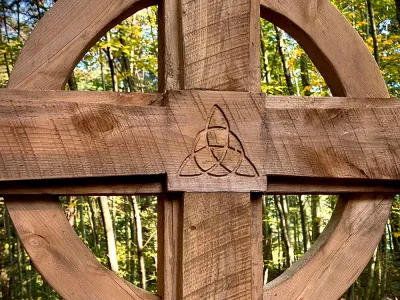 A wooden cross with the green Trinity Forest behind it