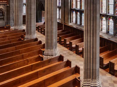 An overhead shot of wooden pews in Trinity Church lining a large wall of stained glass windows with light shining through