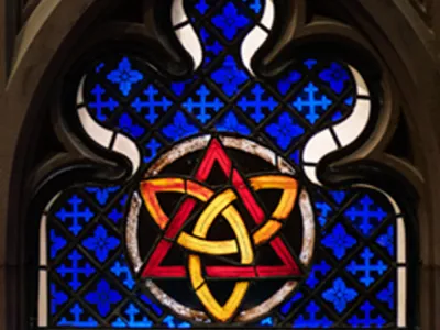A stained glass window featuring a gold trinity knot inside a red triangle over a blue backdrop
