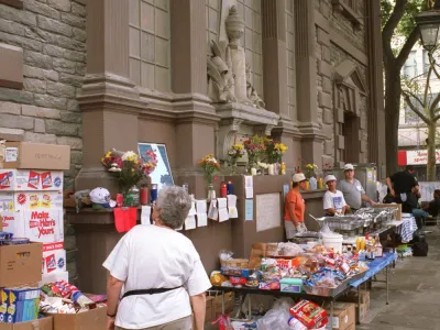 Volunteers serve hot food amidst boxes of donated food and memorial flowers