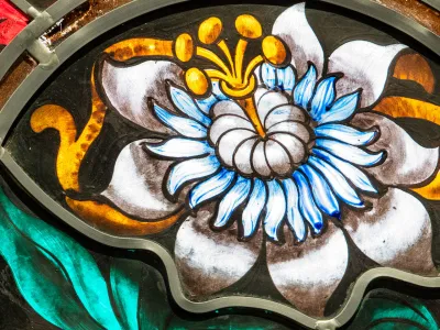 Stained glass image of a large white flower surrounded by green leaves