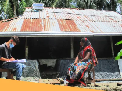 Image of two people sitting across from each other in front of a house with corrugated metal roof.