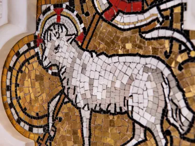 A mosaic of a lamb made up of white, gold, and red tiles on an altar