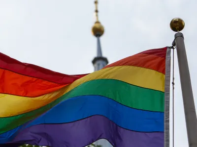Pride flag hoisted in front of St. Paul's Chapel, with the steeple in the background.