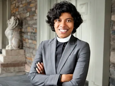 The Rev. Winnie Varghese stands on a porch in front of St. Mark's.