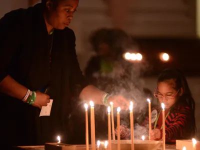 A woman lights a tall, thin candle during a community prayer service