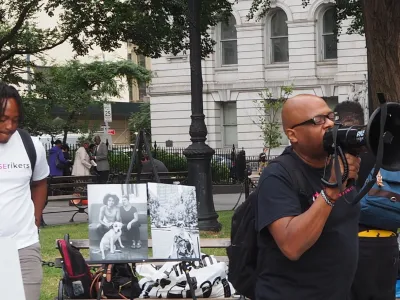 Close Rikers protest in front of City Hall. A man with locs looks down in the background, while another bald man in glasses holds a megaphone. 