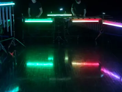 Rainbow lights in a dark space where percussionists are playing.