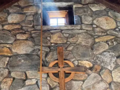 Beam of light coming in through a small window in a stone wall of the Retreat Center chapel, above a wooden cross