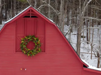 The red, wooden Retreat Center barn, decorated with a wreath, in front of snowy woods