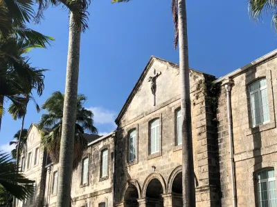 An exterior shot of Codrington College in Barbados, January 2020. The palm trees in the foreground sway to the left.