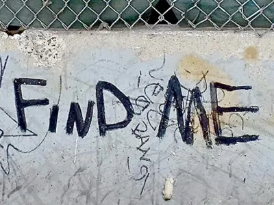 The words "Fine Me" painted in black on a cement barrier in the street