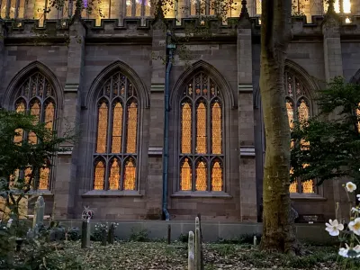 Golden light shines from within Trinity Church and lights up the windows, as seen from Trinity Churchyard on an autumn evening