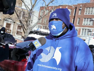 A masked representative from the Fortune Society speaks into a News12 microphone.