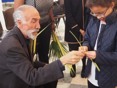 A man shows a little girl how to make a palm cross