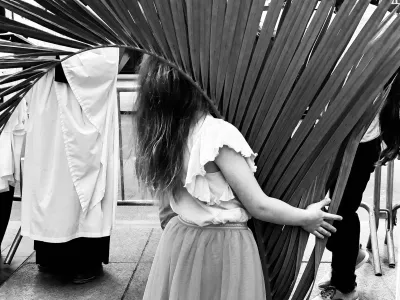 A child carries a large palm branch in a black and white photograph