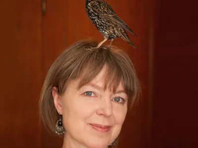 Portrait of Lyanda Lynn Haupt with a bird standing on her head.