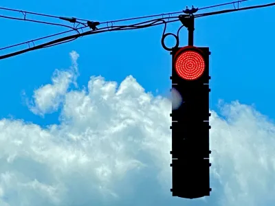 Photo of a red stoplight and a bright blue, cloud-filled sky