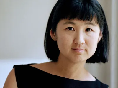 Maya Lin faces the camera wearing a black boatneck top in front of a white backdrop. 