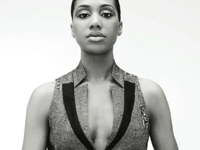 LaToya Ruby Frazier looks directly at the camera with her hair slicked back in a black-and-white photo. She wears a vest that has stylized lapels.