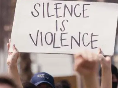 Protest on the Brooklyn Bridge, hands holding a white cardboard sign that says "Silence is Violence," written in capital letters with a thick black marker.