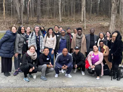 A multiethnic group of people wearing coats, scarves, and other outerwear smile for a group photo outside the Trinity Woods in West Cornwall, Connecticut.