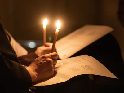Two people holding slim candles, their hands resting on bulletins.