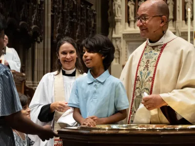 A young baptismal candidate stands at the font with Father Phil and Mother Kristin