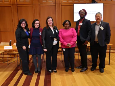 Six panelists of varying ethnic and racial background stand in a row, smiling at the camera. The screen behind them says "Mental Health Symposium: Impact of Food Insecurity on Emotional Well-Being"