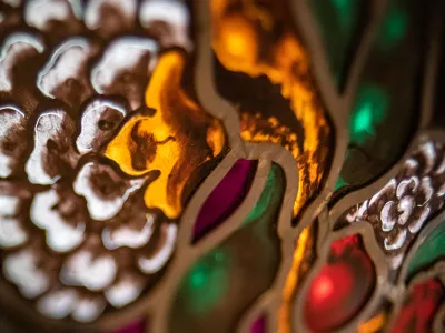 Close-up photograph of a stained-glass window depicting a flower with white, gold, green, red, and burgundy