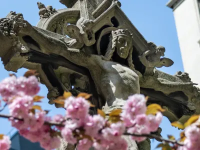 A brach of blooming pink flowers in front of the Astor cross in Trinity Churchyard