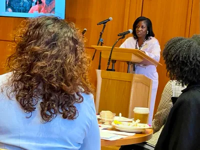 Tasha Tucker speaks at a podium in front of guests in Parish Hall.