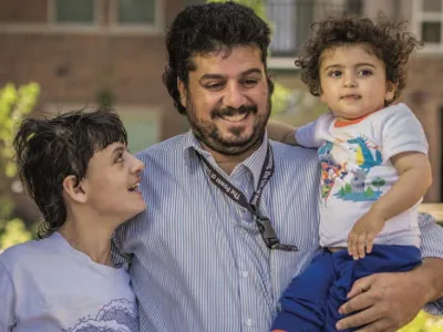 A smiling father holds his two children outside an Enterprise Community Partners property.