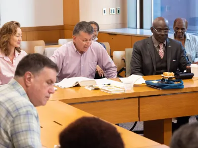 Adults meet around a wooden desk to discuss scripture.