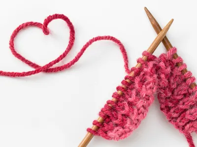 Image of knitting needles with pink yarn in the shape of a heart