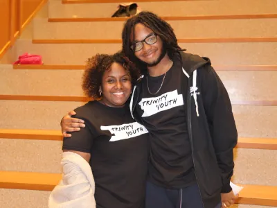 Trinity Youth staff Jayla Allen and participant smile by the staircase at the Trinity Commons lower level lobby.