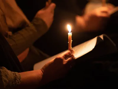 A person holds a glowing, burning candle on their hand during a vigil service at Trinity Church