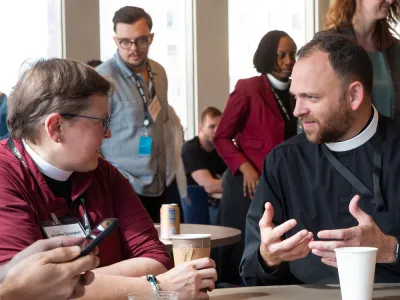 Two priests talk to one another while seated at a table.
