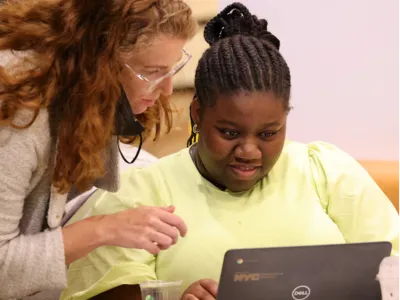 Jenn Chinn assists a young woman using a laptop.