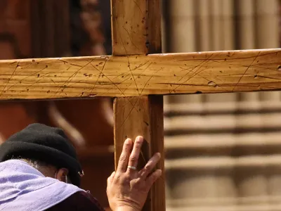 A person bends before and places their hand on a wooden cross in Trinity Church