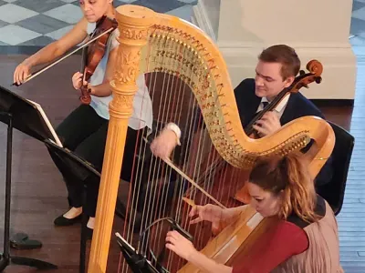 Three musicians play instruments, from the left: violin, cello and harp