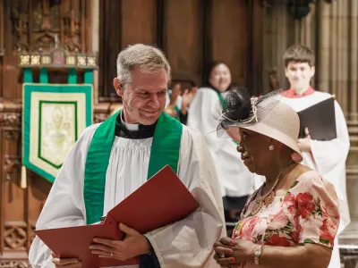 Father Michael Bird stands with a parishioner near the front of the Trinity Church with the choir standing in the background