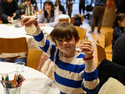 A child smiles and holds up a handmade Christmas tree ornament