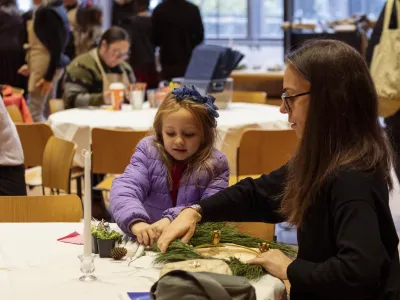A girl makes a Christmas wreath with a lady.