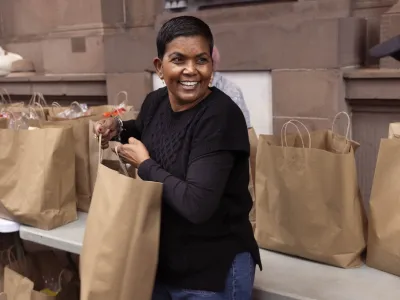 A lady distributes grocery bags to people in line.